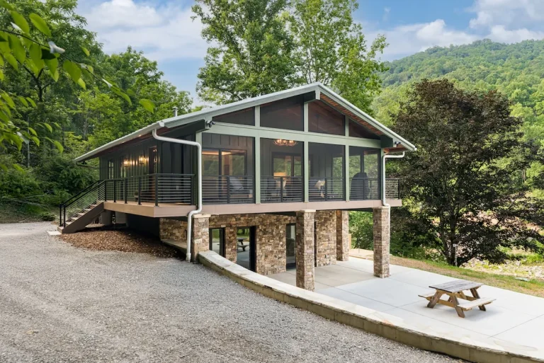 Elevated green home with screened porch and stone base.