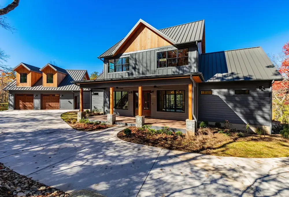 Modern farmhouse with dark board-and-batten siding, a metal roof, a timber-post front porch and a detached two-car garage.