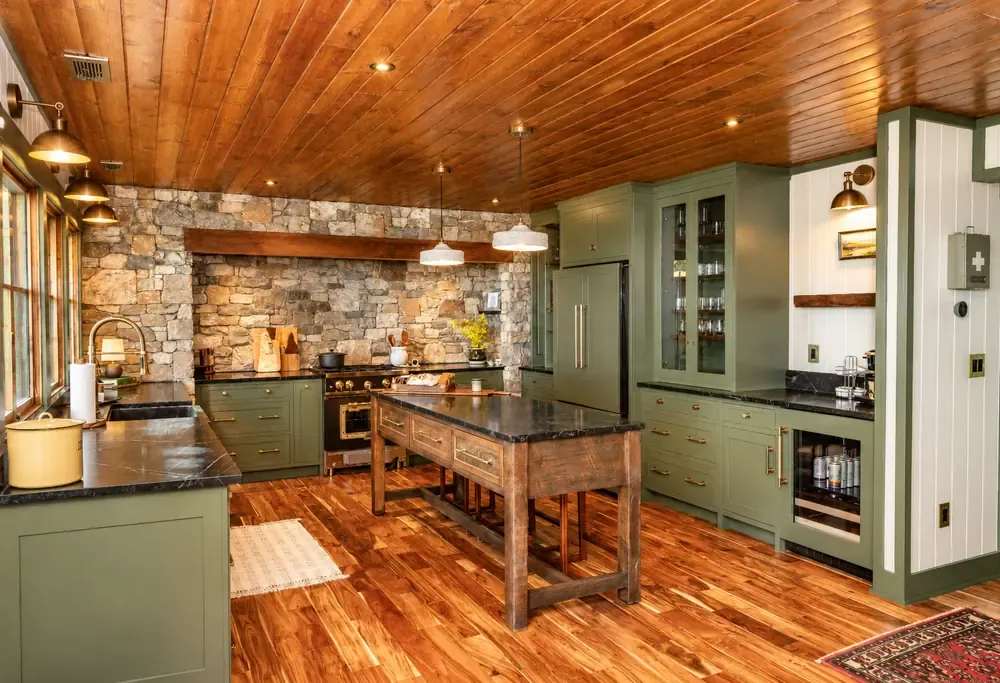 Kitchen with sage green cabinets, a stone accent wall, black stone counters, a wood plank ceiling and a rustic wood island.