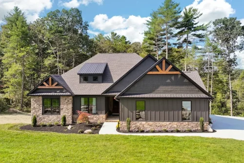 Dark-sided home with stone accents, timber details beneath the roof peaks, and a covered front entrance, surrounded by lawn and trees.