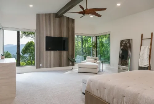 Bedroom with large corner windows, mountain views, a wood slat accent wall, and modern ceiling fan.