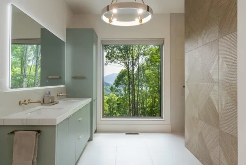 Modern bathroom with green cabinetry, a double vanity, geometric tile wall, and large window overlooking the mountains.