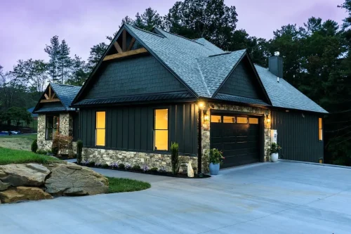 Side view of the home with an attached garage, stone accents, glowing windows, and a wide concrete driveway.