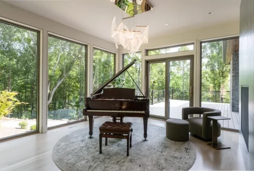 Bright music room with a grand piano, floor-to-ceiling windows, and doors opening to an outdoor deck