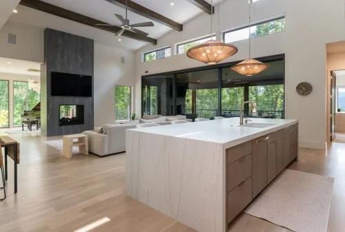 Open-concept kitchen and living area with a large waterfall island, vaulted ceiling, exposed wood beams, and fireplace.