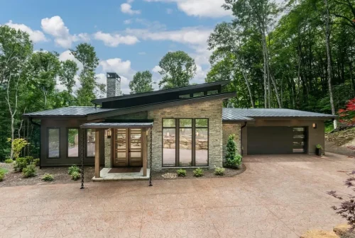 Front exterior of a contemporary mountain home with stone accents, dark siding, metal roof, and attached garage.