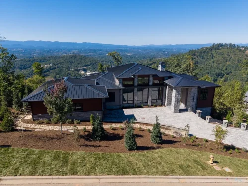 Contemporary mountain home with a dark metal roof, stone and wood exterior, landscaped front yard, and expansive mountain views.