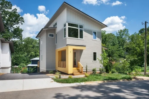Modern two-story home with gray siding, large windows, and a yellow front porch accent.