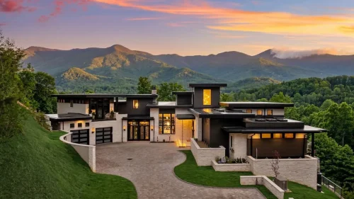 Contemporary mountain home at sunset with layered rooflines, stone and dark siding, multiple garages, and expansive mountain views.