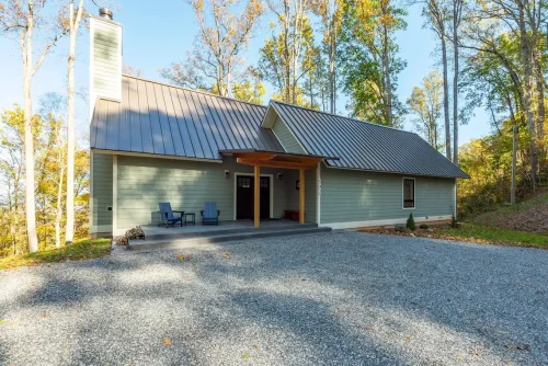 Exterior of a green mountain home with a metal roof and covered front entry surrounded by trees.