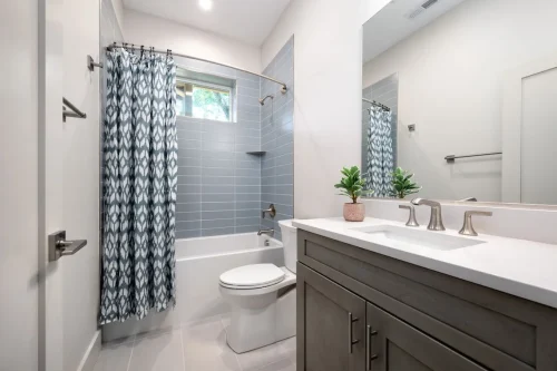 Basement bathroom with gray vanity, white countertop, tub with blue tile surround, and patterned shower curtain.