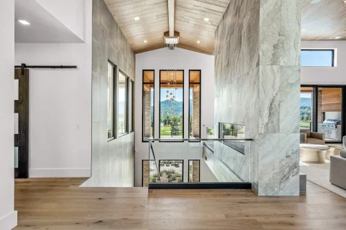 Interior hallway with tall windows and modern light fixture, opening to mountain views beyond.
