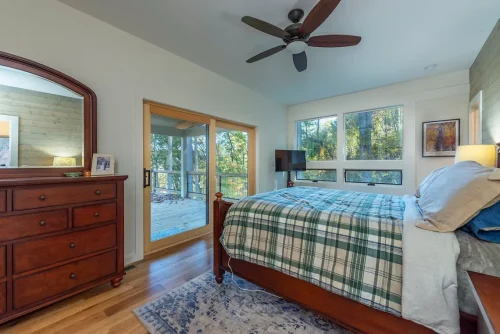 Primary bedroom with hardwood floors, large windows, and sliding glass doors opening to a covered deck.