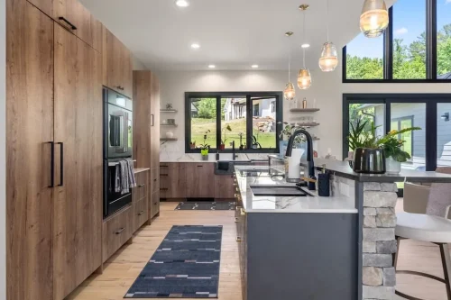 Modern kitchen with wood cabinetry, a large island, stone countertops, pendant lighting, and black-framed windows.
