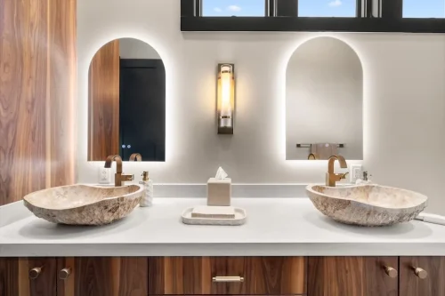 Double vanity with wood cabinetry, stone vessel sinks, arched mirrors, and brass fixtures.