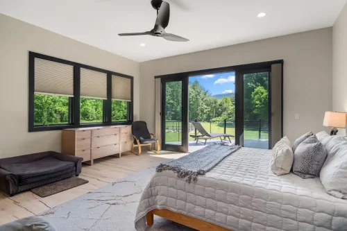Bedroom with large black-framed windows, patio access, wood flooring, and views of the surrounding landscape.