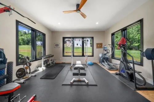 Exercise room with weight-training and cardio equipment, large windows, and rubber flooring.