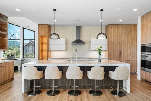 Sleek modern kitchen with large marble island, wood cabinetry, pendant lights, and high-end appliances.
