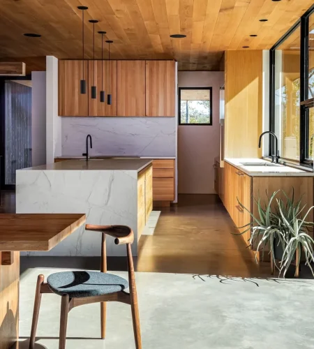 Kitchen with light wood cabinetry, stone island, and black pendant lighting