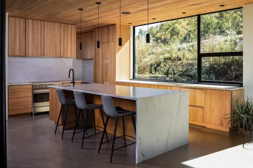 Open kitchen with large island, wood finishes, and expansive window framing a garden view