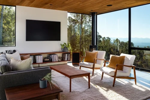 Living room with mid-century furniture, wood accents, and floor-to-ceiling windows overlooking mountains