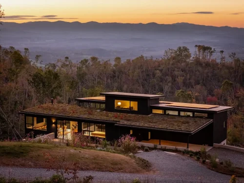 Hillside home at sunset with illuminated interior and mountain landscape backdrop