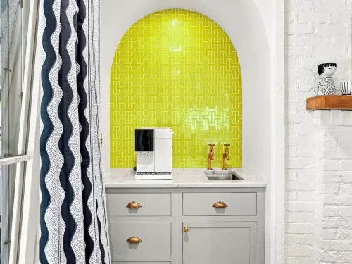 Arched coffee station with gray cabinetry, brass fixtures, and a bright green patterned tile backsplash.
