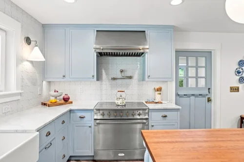 Light blue cabinetry with a stainless steel range, white patterned backsplash, and brass accents.