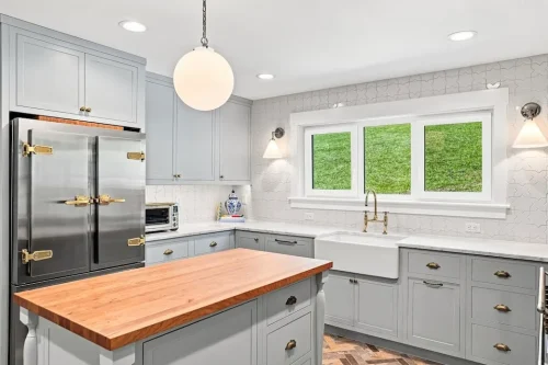 Light blue kitchen with a butcher-block island, farmhouse sink, stainless steel refrigerator, and brass hardware.