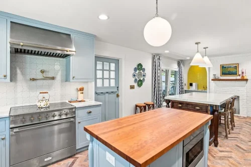 Kitchen with light blue cabinetry, butcher-block island, stainless steel range, and a large marble-topped island.