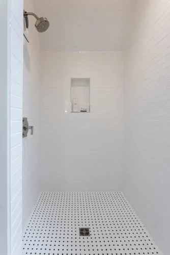Walk-in shower with white tile walls, built-in niche, and black-and-white tile flooring.