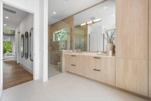 Bathroom with double vanity, glass shower, and light wood cabinetry.