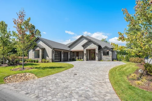 Modern stone and wood home with driveway and landscaped yard.