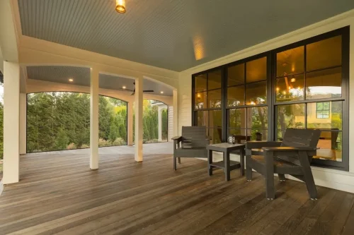 Spacious covered porch with wood decking, arched openings, outdoor seating, and black-framed windows.