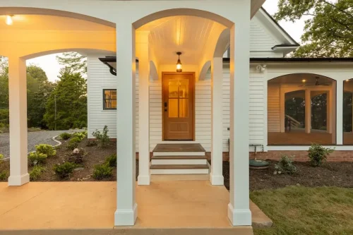 Covered entry walkway with white columns, arched openings, wood door, and adjoining screened porch.