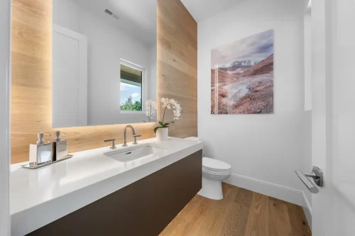 Powder room with backlit mirror, wood accent wall, and minimalist design.