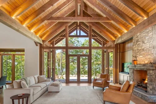 Open living room with soaring wood-beamed ceiling, stone fireplace, large windows, and cozy seating arranged to highlight mountain views.