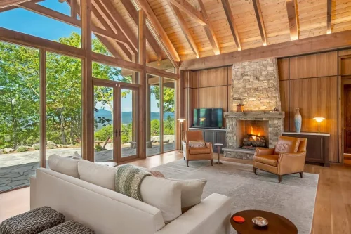 Rustic yet elegant living space featuring a stone fireplace, leather chairs, and expansive glass doors framing views of the Blue Ridge Mountains.