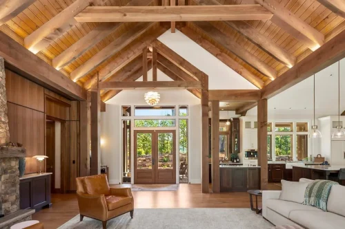 Vaulted living room showcasing timber beams, stone fireplace, and open flow into the modern kitchen and dining area.