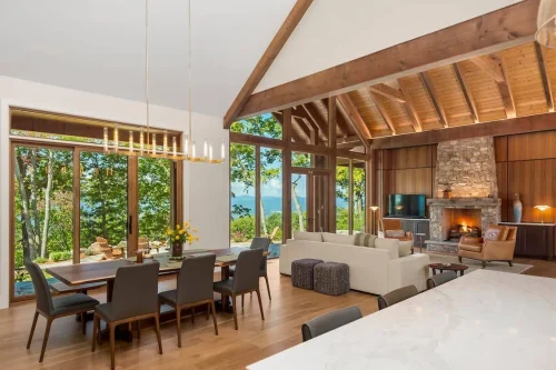 Open dining and living area with long dining table, stone fireplace, and full wall of windows overlooking the mountains and patio.