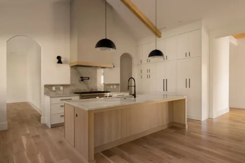 Modern kitchen featuring a light wood island, white cabinetry, marble countertops, black pendant lights, and arched doorways