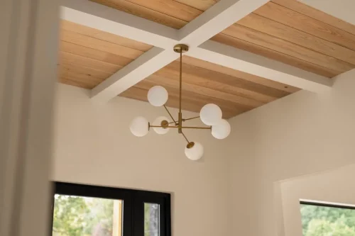 Wood-paneled ceiling with white beams and a modern brass chandelier featuring round white glass globes.