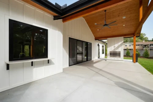 Spacious covered patio with a wood-paneled ceiling, black-framed sliding glass doors, outdoor fireplace, and ceiling fan.