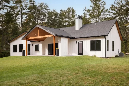 White board-and-batten home with black windows, a dark roof, wood accents, and a covered patio overlooking the lawn.