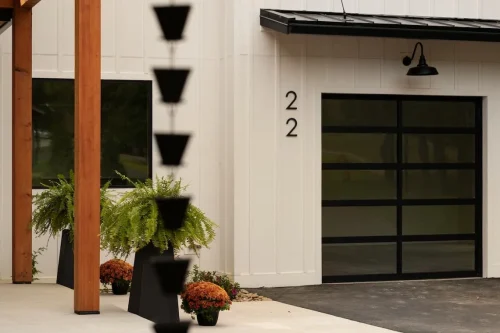 Close-up of the home's white board-and-batten siding, black glass garage door, wood porch posts, and decorative landscaping.