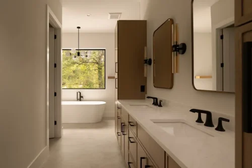 Spacious bathroom with a double-sink vanity, light wood cabinetry, black fixtures, and a freestanding bathtub beneath a large window.