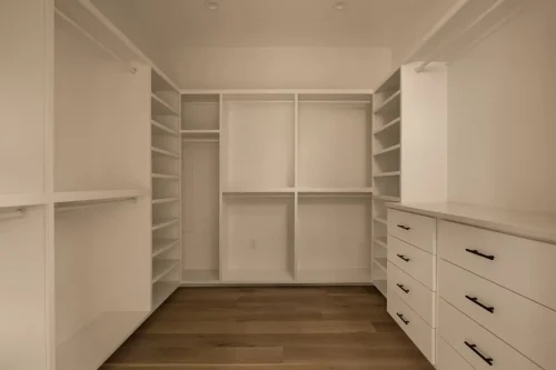 Walk-in closet featuring white built-in shelving, hanging rods, storage drawers, black hardware, and wood flooring.
