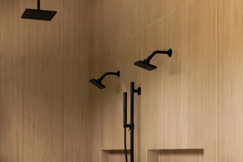 Walk-in shower featuring vertically textured beige tile, multiple matte black showerheads, and recessed storage niches.