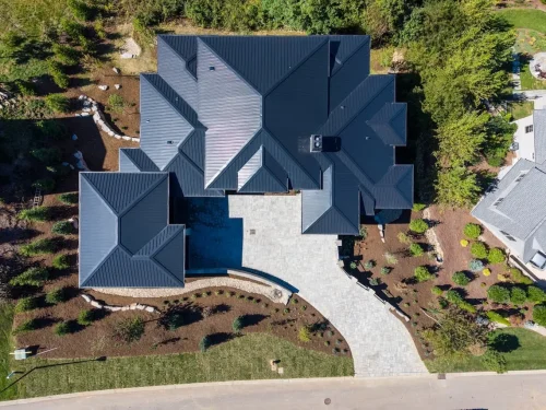 Overhead view of the home showing its multiple rooflines, driveway, landscaping, and surrounding wooded property.