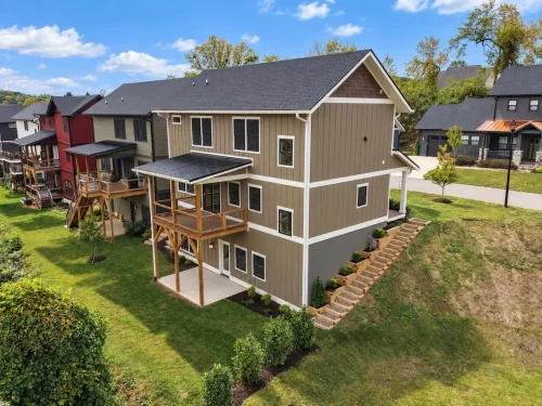 Aerial rear view of the home with a covered deck, lower patio, and landscaped yard.
